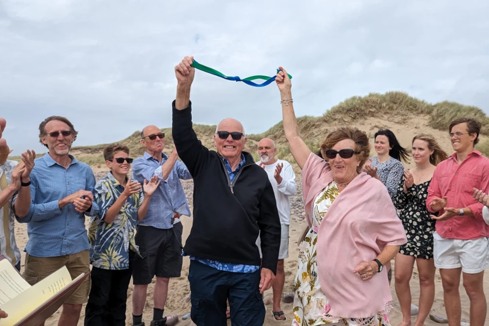 A group of people are holding up a ribbon on the beach.